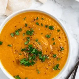 a white bowl of creamy carrot ginger lentil soup garnished with parsley