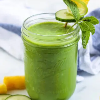 a pineapple cucumber smoothie green smoothie in a mason jr with a cucumber, lime, pineapple, and mint garnish
