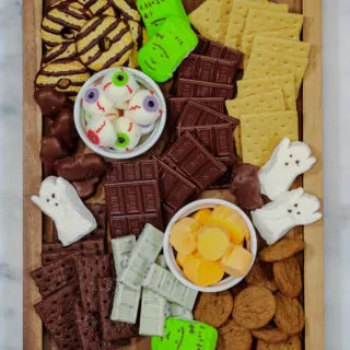 a halloween smores board with various chocolates and candies, halloween-themed marshmallows, graham crackers, and cookies.